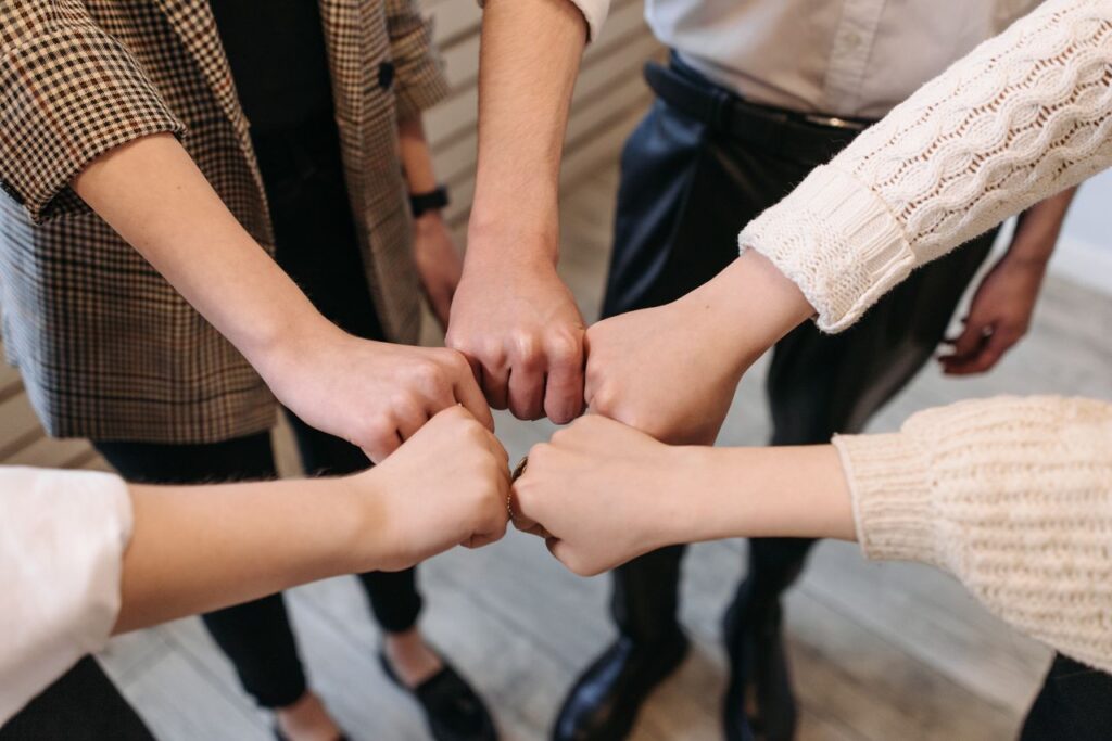 Join Us Five people uniting hands indoors, symbolizing teamwork and unity.